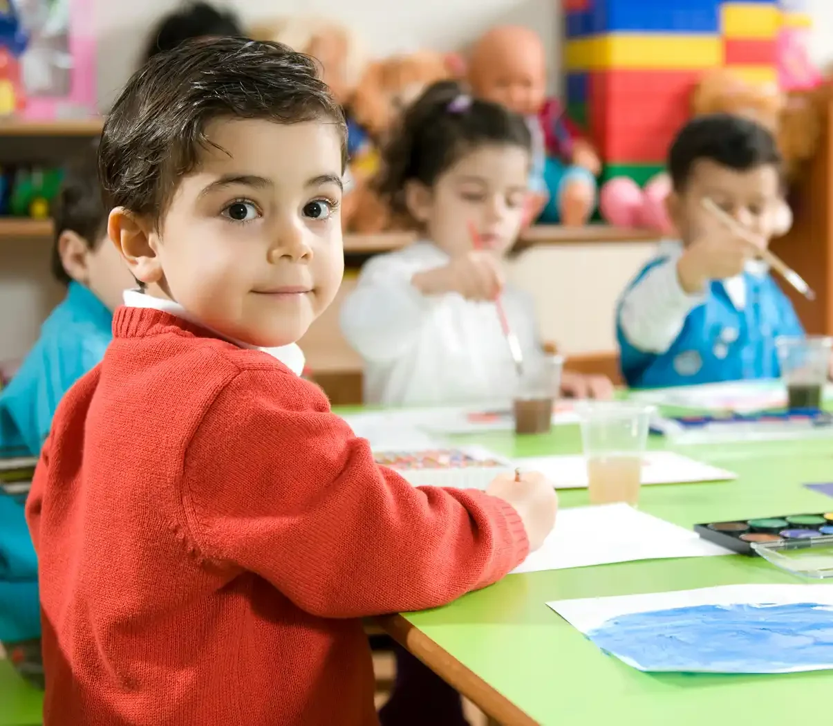 A group of nursery children painting together at a table, representing what to look out for when you apply for a nursery placement.
